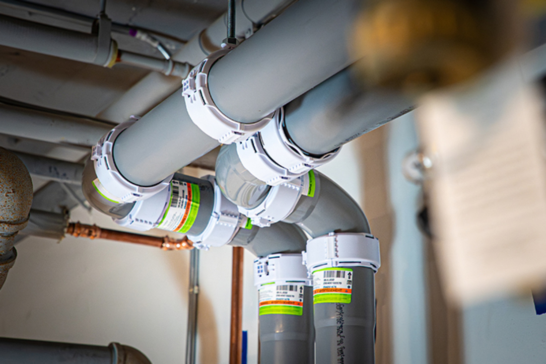 Worker in a high-visibility vest holding a gray innoflue pipe fitting during a  system installation.