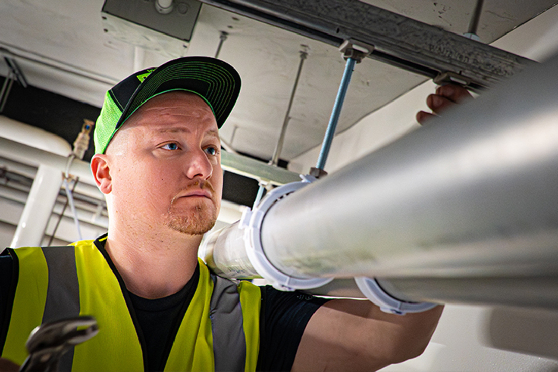 Technician installing suspended innoflue mounted to ceiling supports in a commercial building.