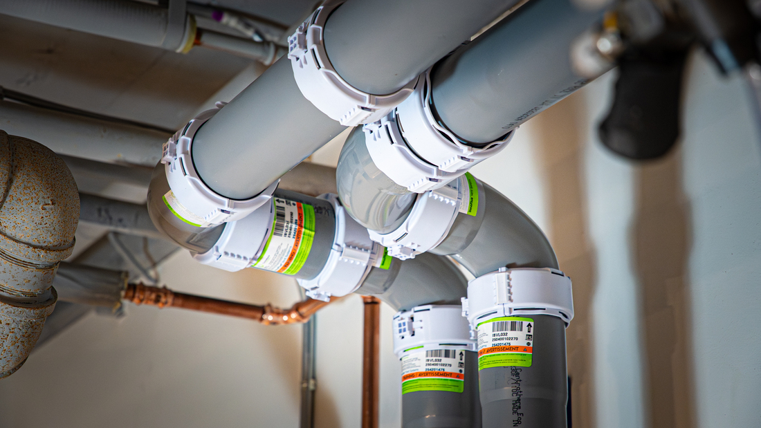 Gray pp pipes with white octoclamps installed beneath a ceiling, with copper and metal pipes visible in the background.