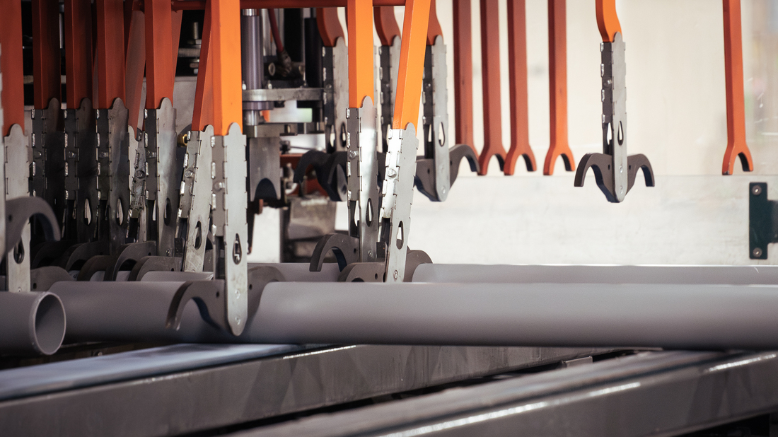 Industrial machinery transporting gray PP pipes along a production line using orange and metal automated gripping arms.